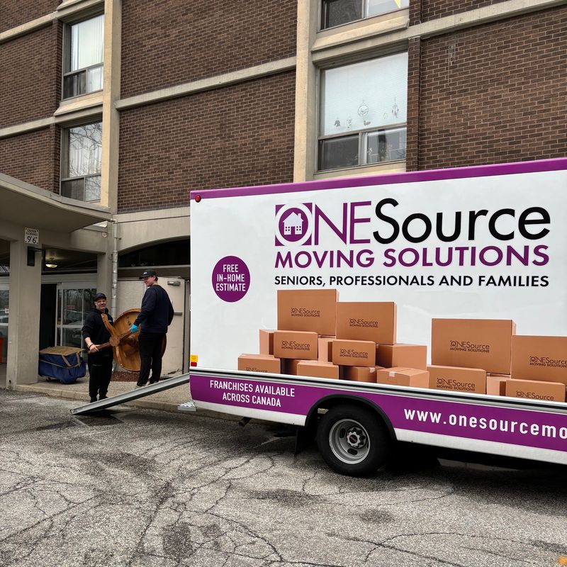 A ONESource truck at the entrance of a brick apartment building, with movers carrying a wooden table down the ramp